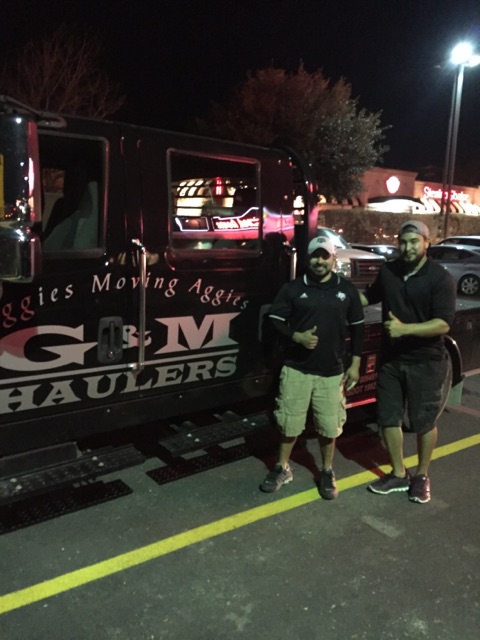 Two men stand at night beside a G&M Haulers truck in a parking lot, both giving thumbs up and smiling at the camera.