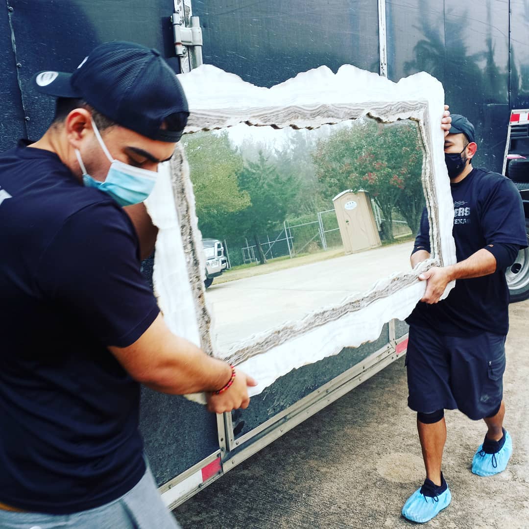 Two people wearing masks and black clothing carry a large, ornate mirror outside near a truck and shed. Two people wearing masks and black clothing carry a large, ornate mirror outside near a truck and shed.