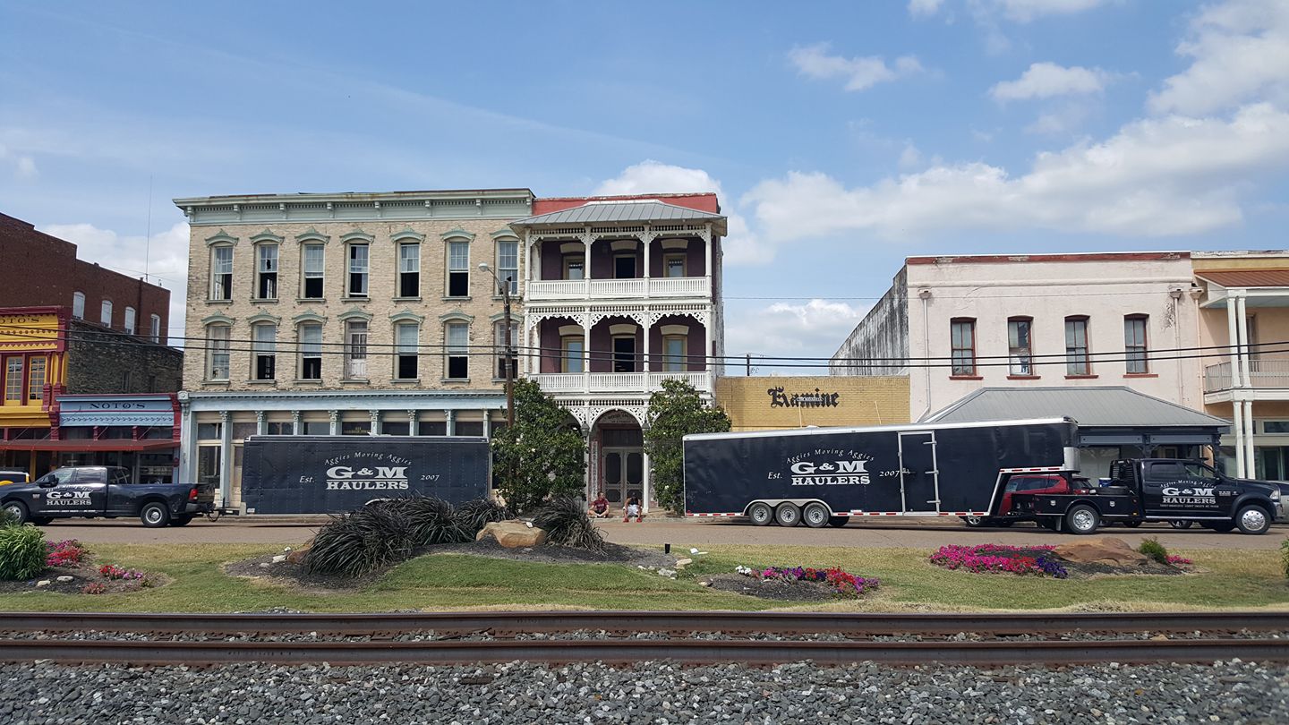 Three large G&M Haulers trucks are parked in front of historic buildings near railroad tracks on a clear day. Three large G&M Haulers trucks are parked in front of historic buildings near railroad tracks on a clear day.